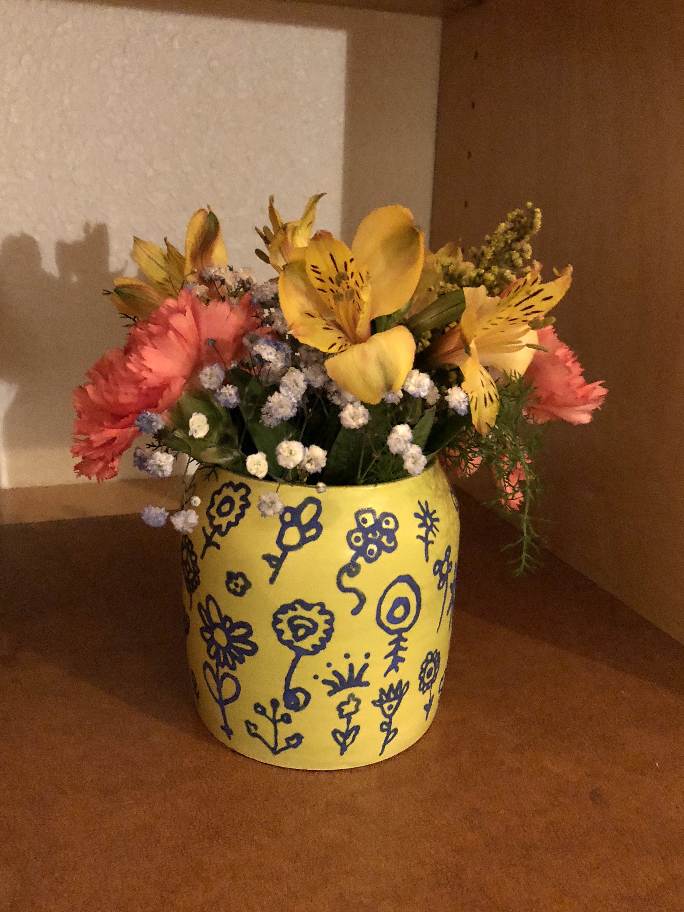 Yellow ceramic vase with drawings on it holding colorful flowers